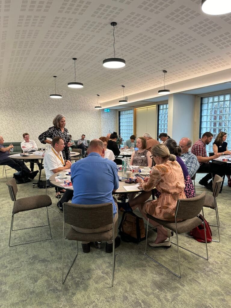 Angella Clarke-Jervoise People seated at round tables in a modern conference room participate in a group discussion or workshop.